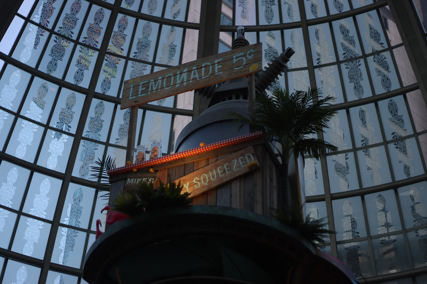 A decorative lemonade stand on top of a high platform under a glass dome.